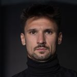 Serious male wearing a black turtleneck sweater, captured in a studio setting with a dark background.